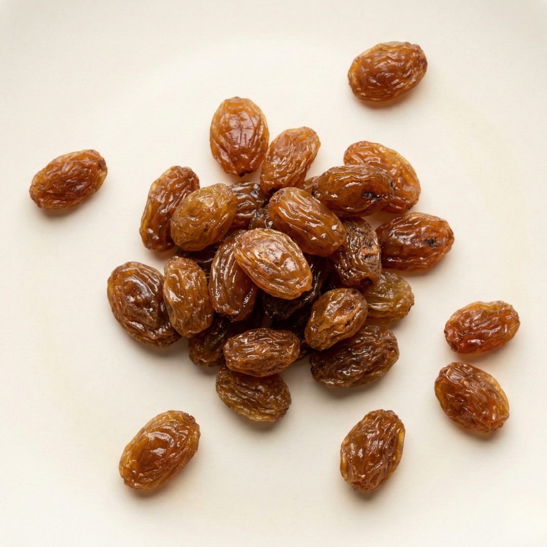 A close-up, overhead shot of a pile of golden raisins on a plain, off-white surface.