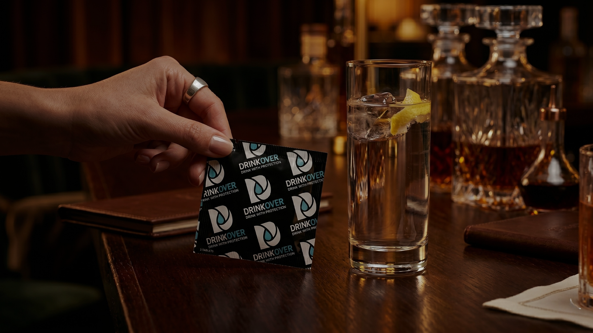 A hand holding a Drinkover packet next to a cocktail on a dimly lit bar.