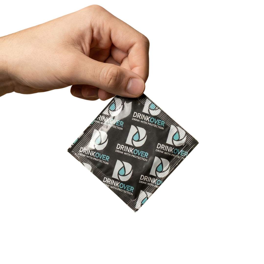 A hand holds a square, black foil packet with the logo for Drinkover against a black background.