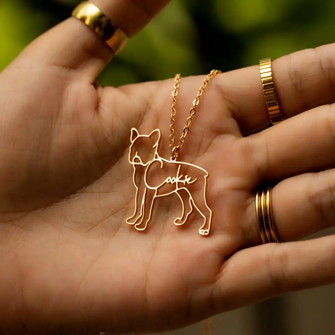 Hand holding a gold dog-shaped pendant with a chain.
