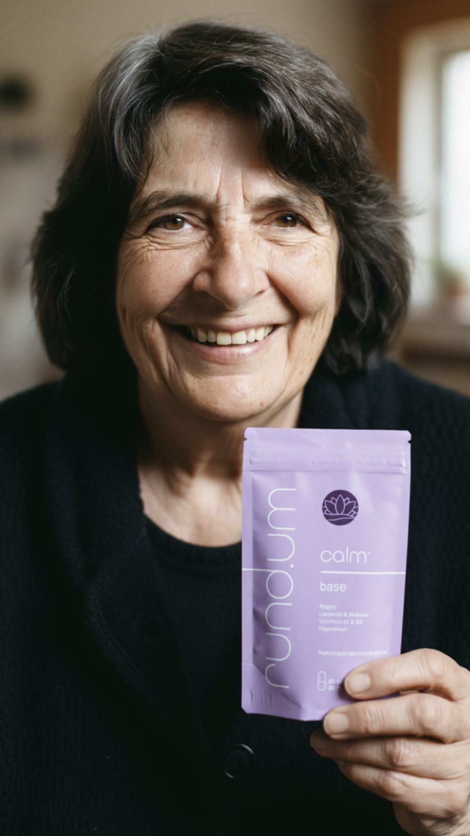 Person smiling, holding black lace underwear in a bedroom.