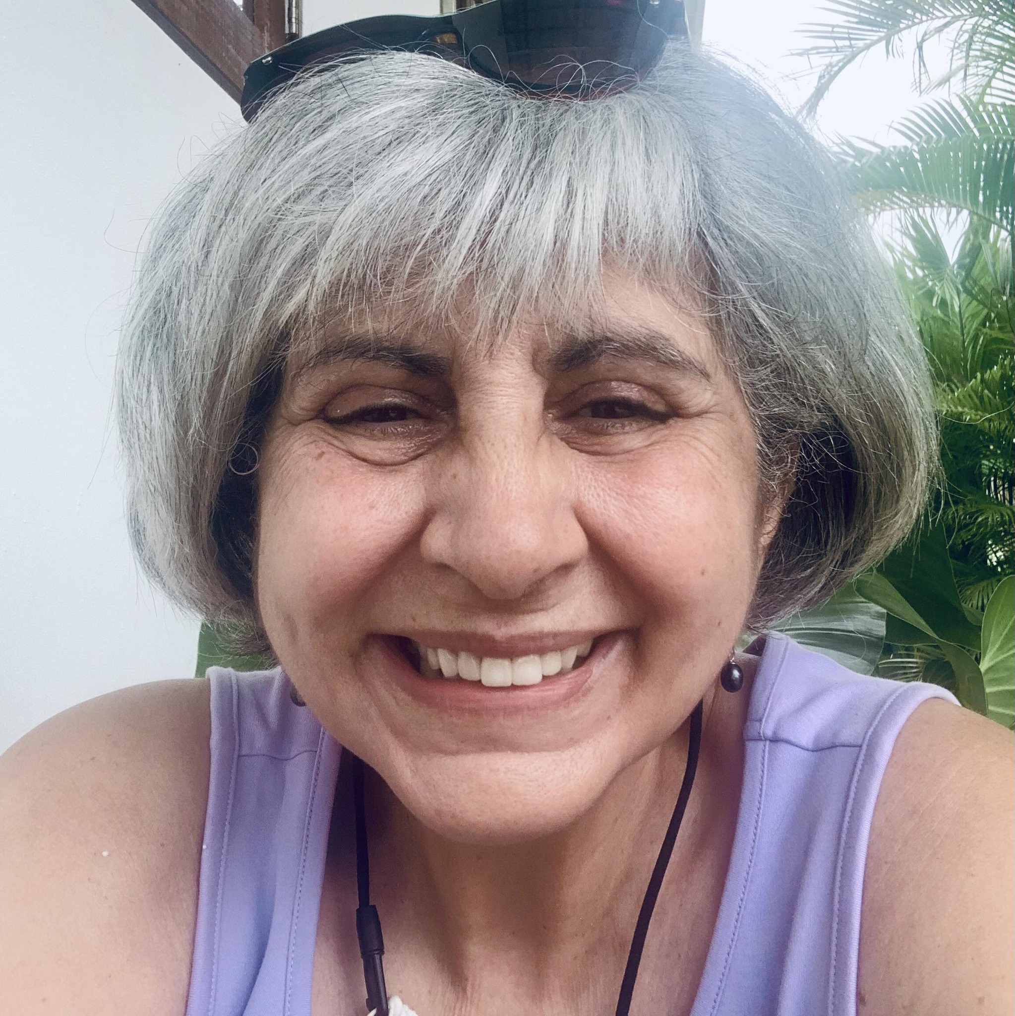 A close-up selfie of a smiling woman with short gray hair in a purple tank top.