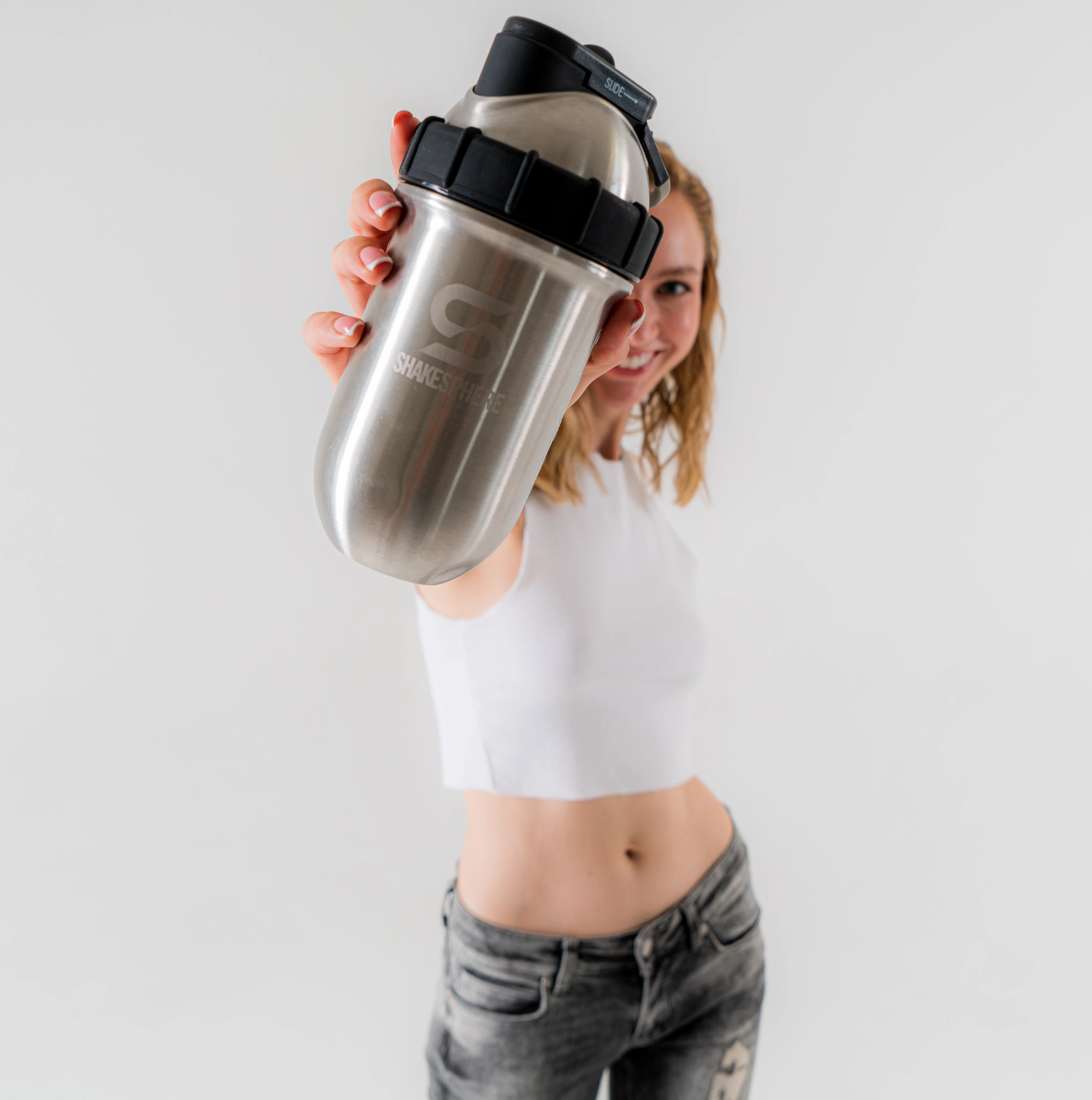 Person holding a stainless steel shaker bottle towards the camera.