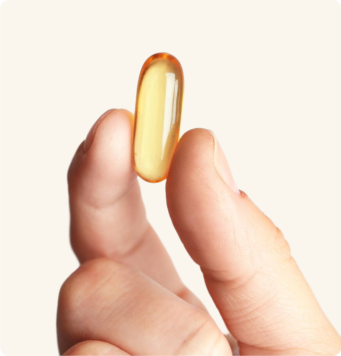 A hand holding a translucent yellow capsule between fingers.