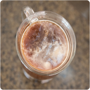Top view of a chocolate milkshake in a glass mug on a textured surface.