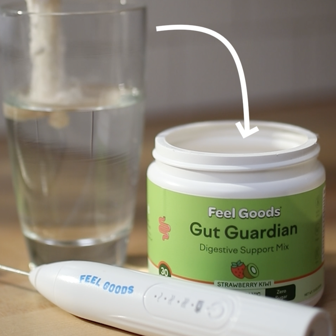 Container of Gut Guardian mix, glass of water, and a mixer on a table.