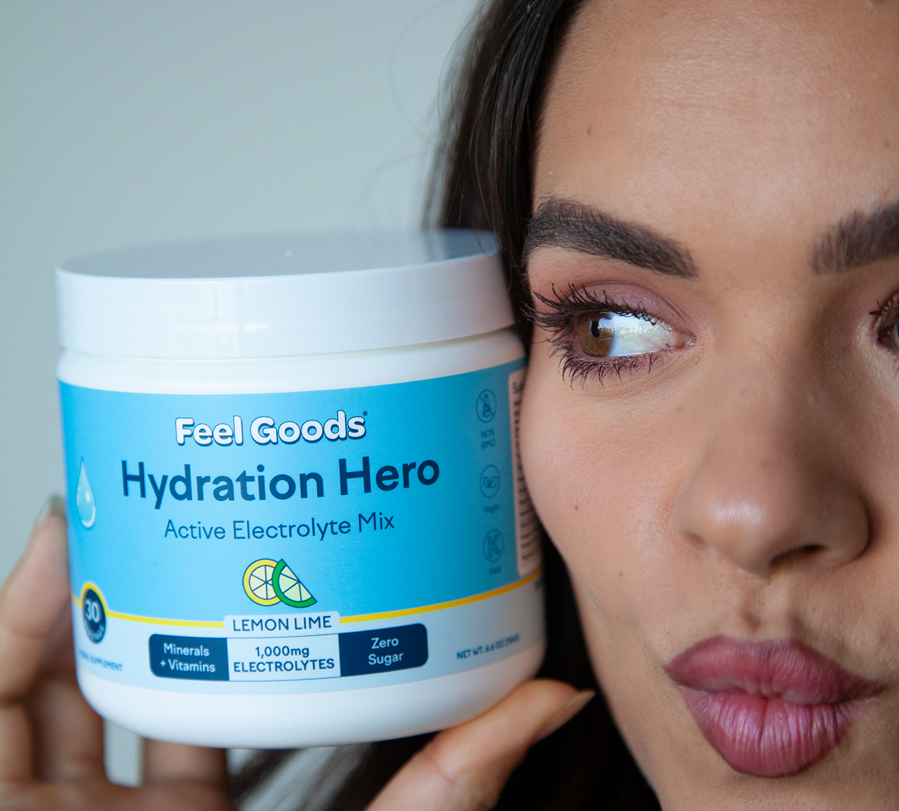 A woman with her eyes closed smiles while drinking a green smoothie in a kitchen, a container of 'Gut Guardian' on the counter.