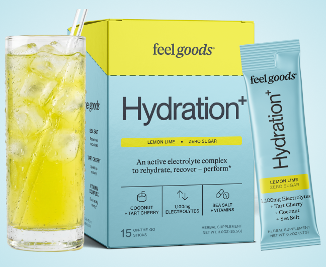 A glass of yellow iced beverage next to a box and packet of feel goods Hydration+ drink mix.