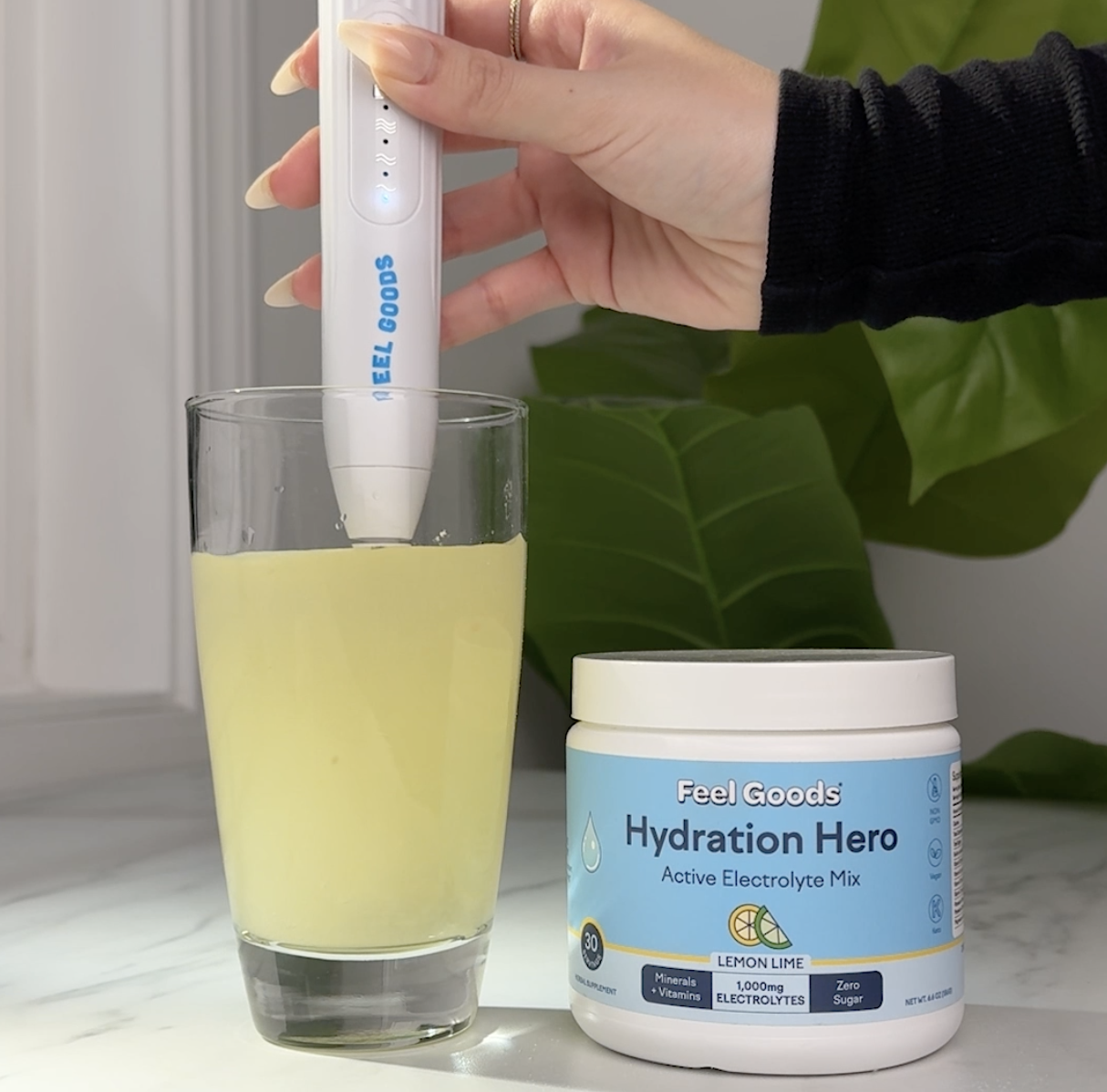 A hand mixing lemon-lime electrolyte drink in a glass with a device.