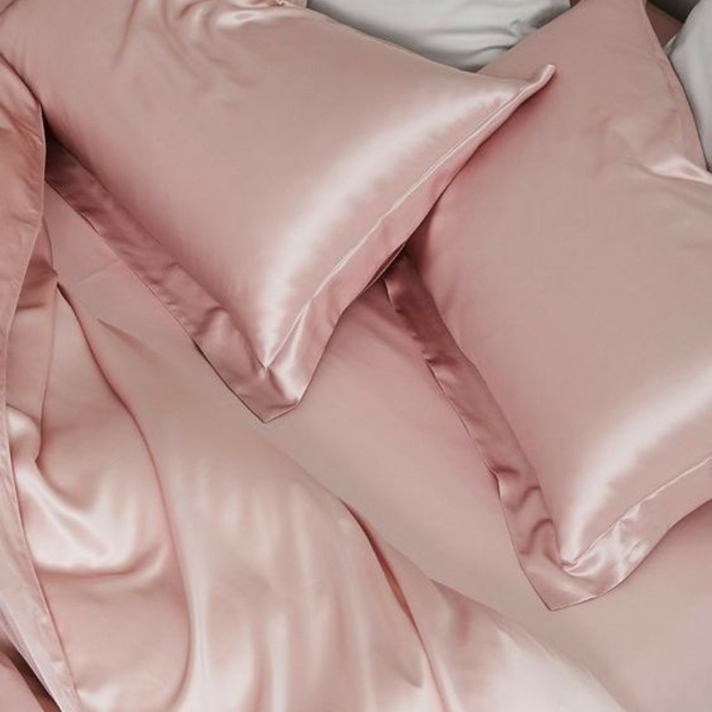 A close-up of rumpled pink silk sheets and pillowcases on a bed.