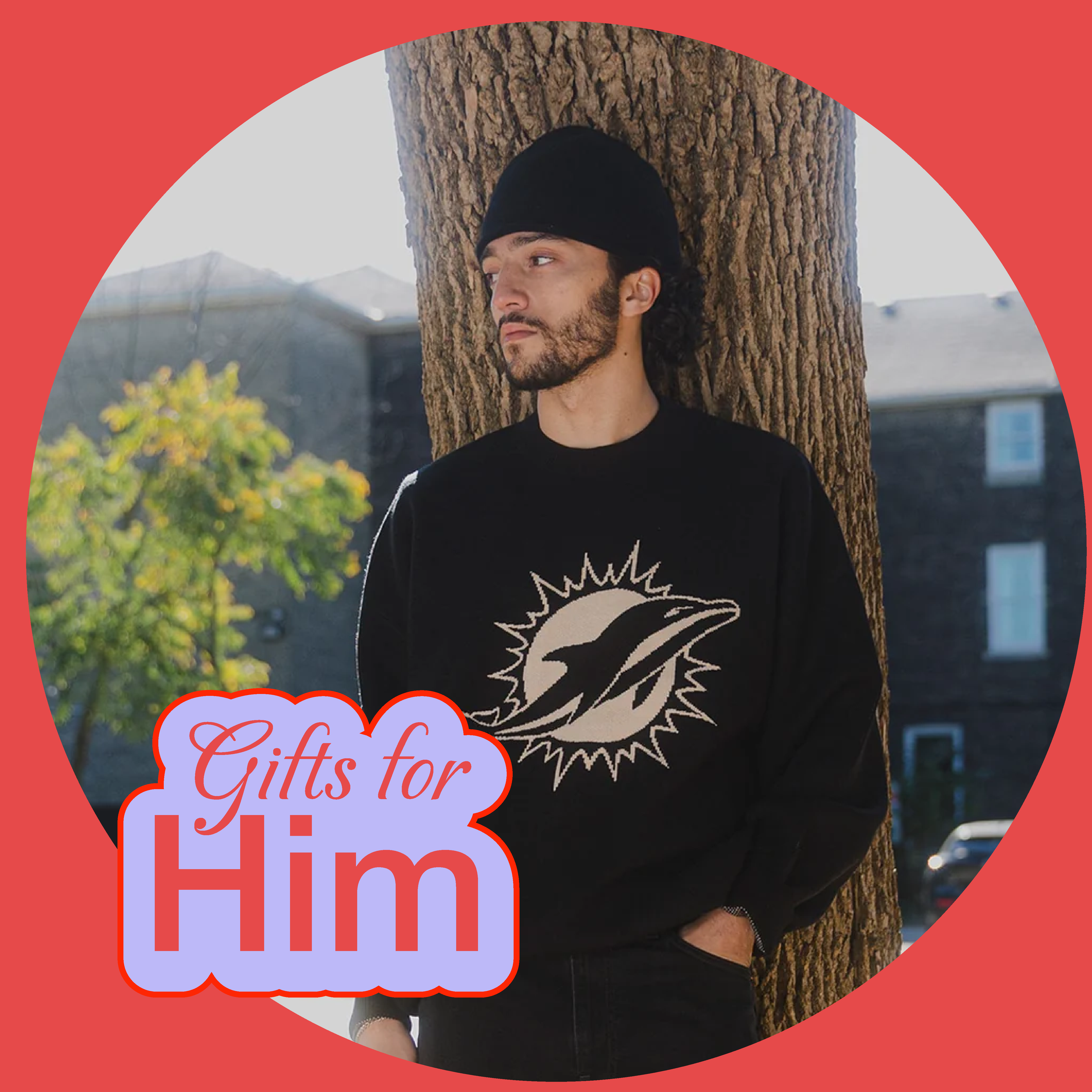 Man in beanie leaning against tree, wearing a sweater with a dolphin logo.