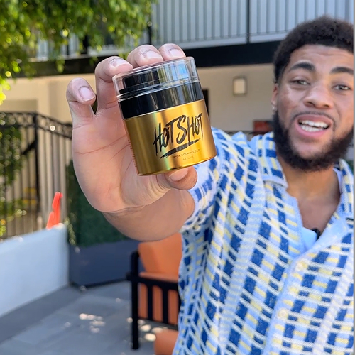 Person holding a gold container labeled 'Hot Shot' outdoors.