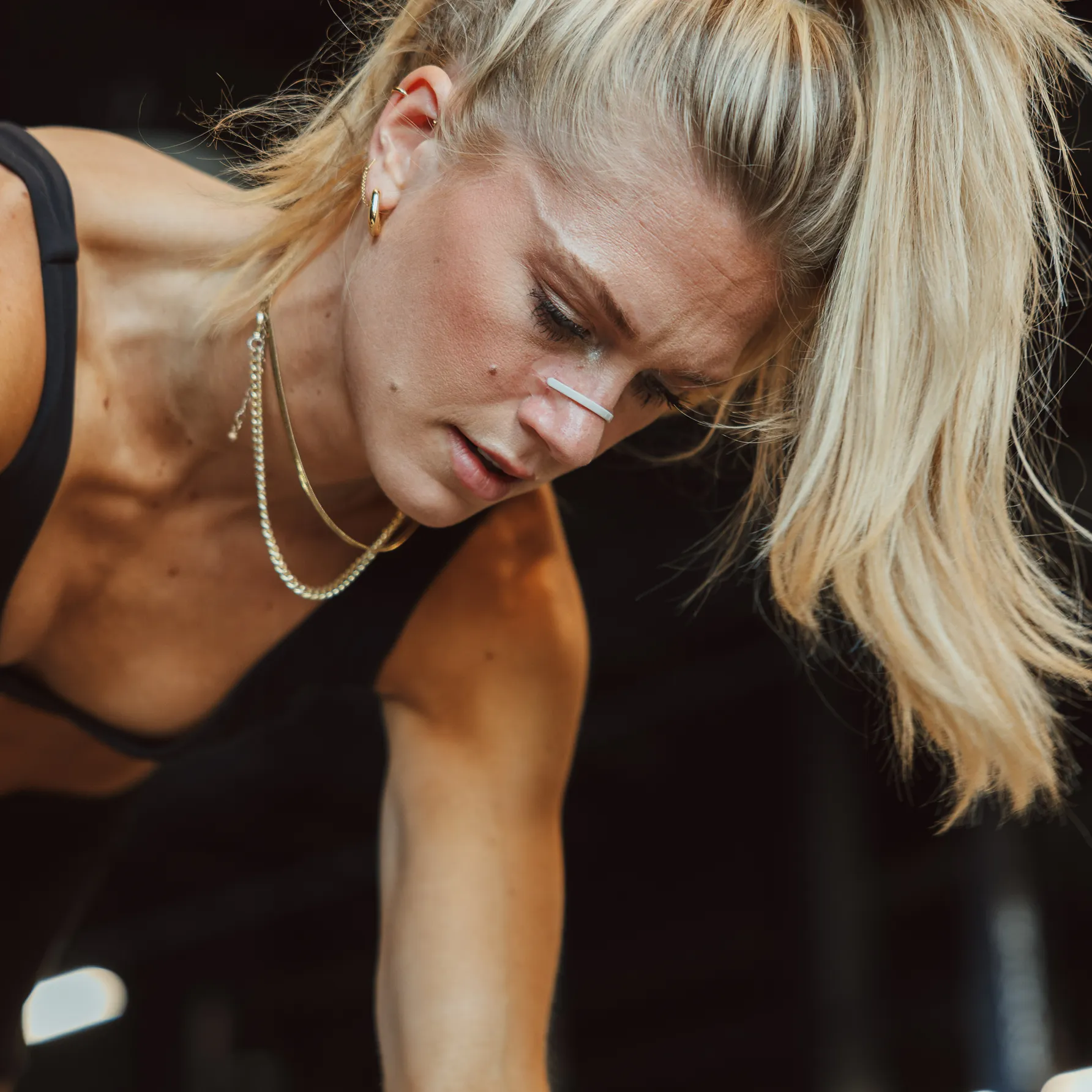 A close-up of a blonde woman wearing a nasal strip, looking down with an expression of concentration.