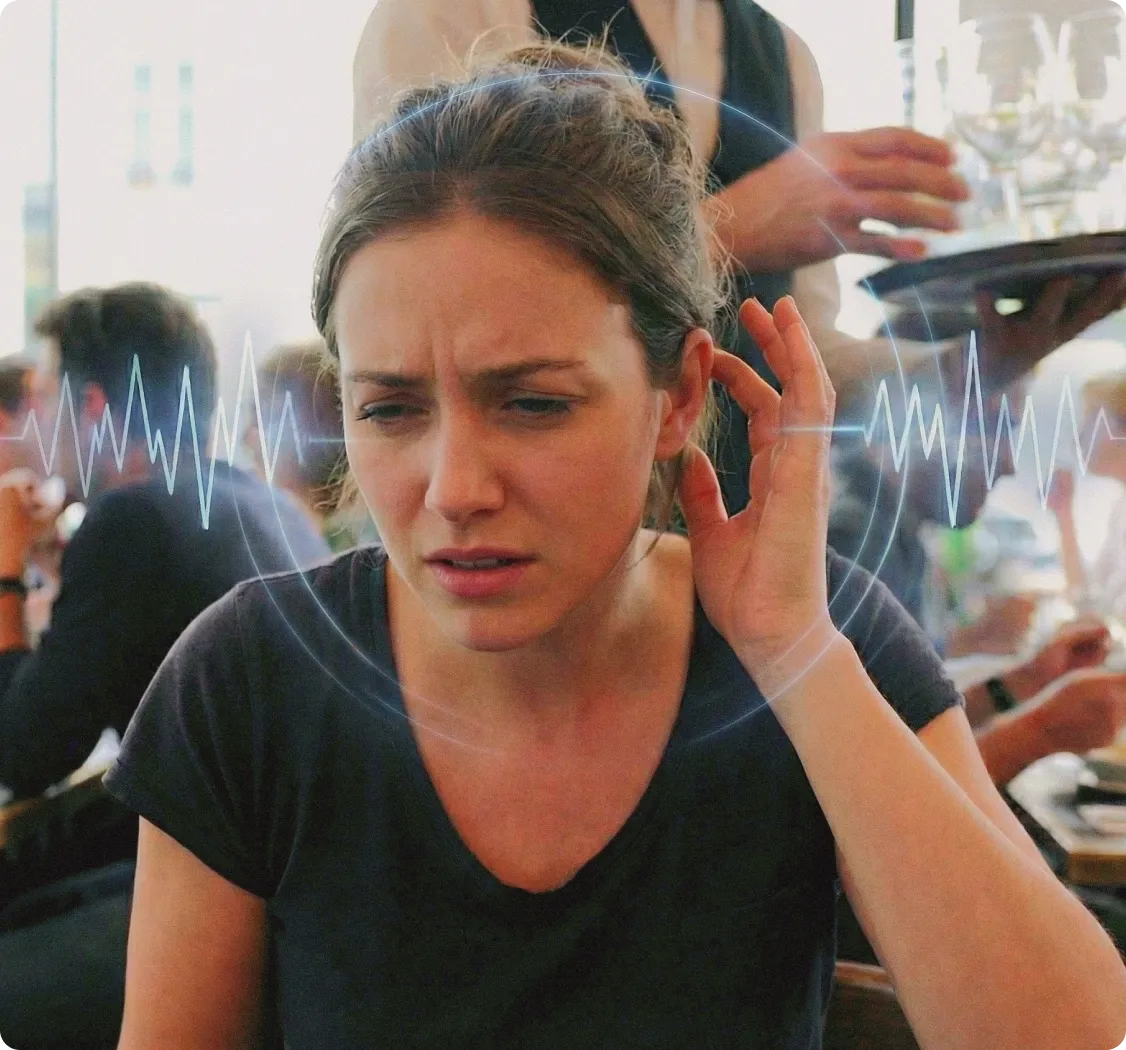 Woman in a cafe holding ear with sound waves visible.