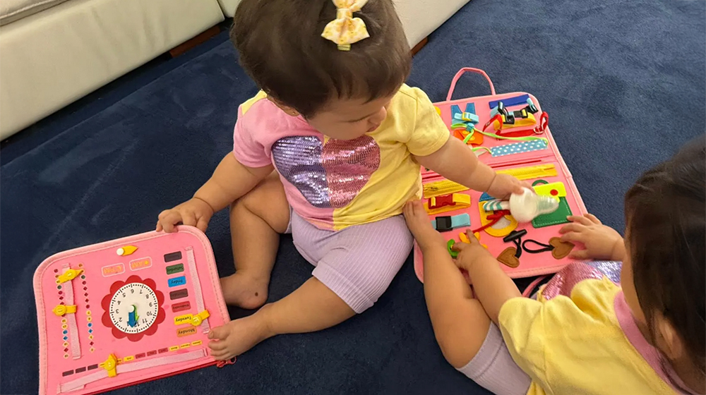 Two children playing with colorful educational activity boards on a blue carpet.