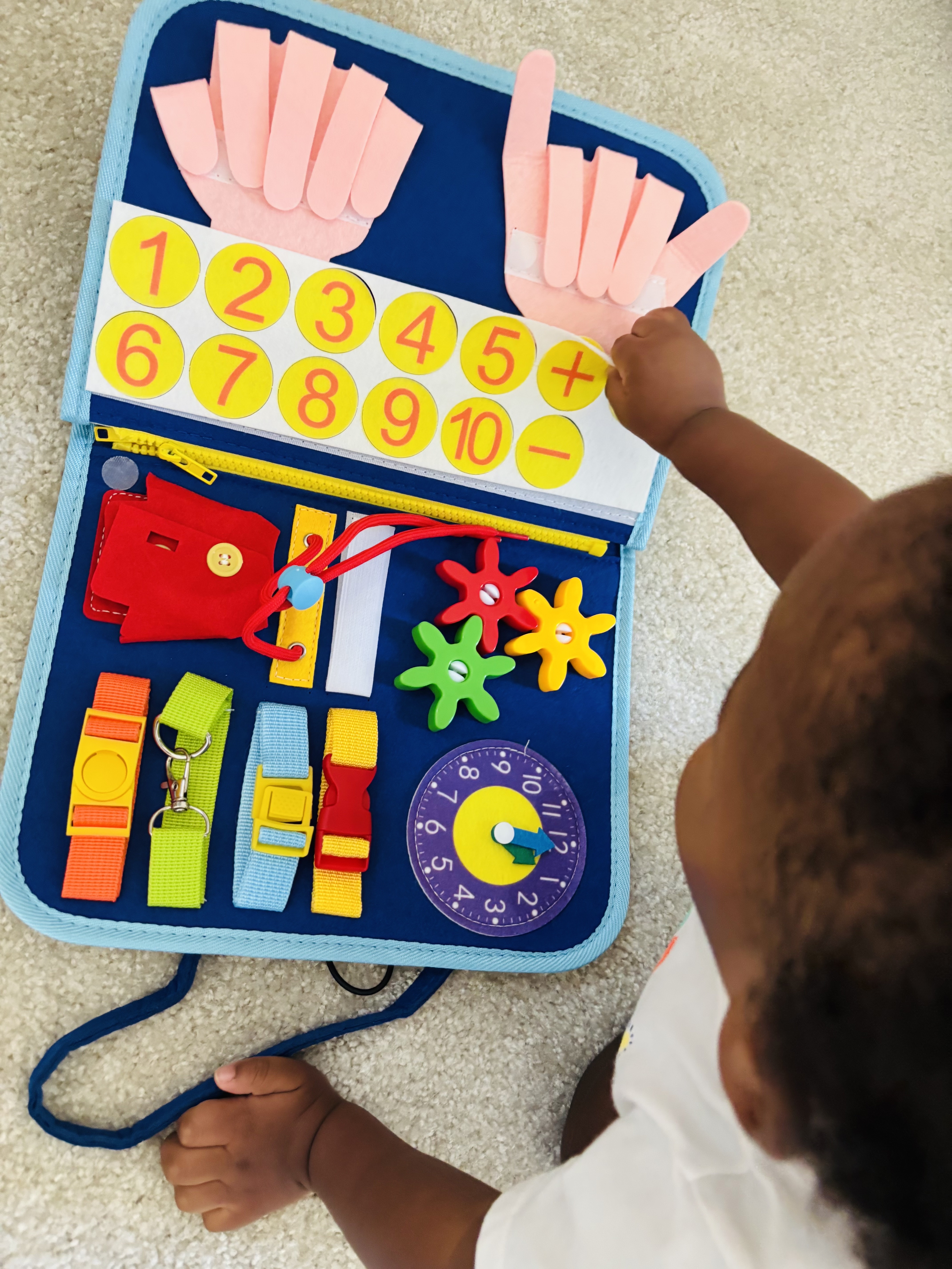 Child playing with an educational activity book featuring numbers, shapes, and colorful fasteners.