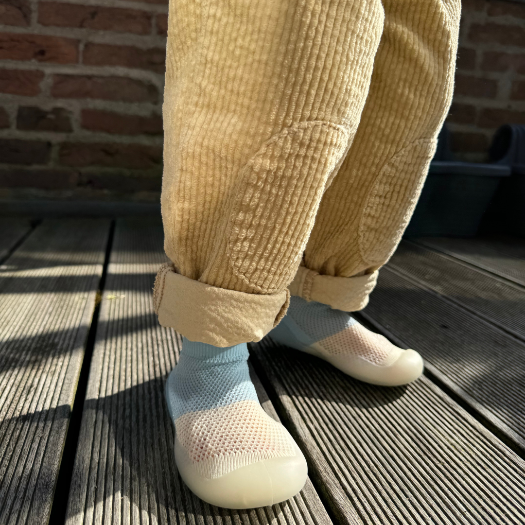 Child wearing beige corduroy pants and colorful socks on a wooden deck.