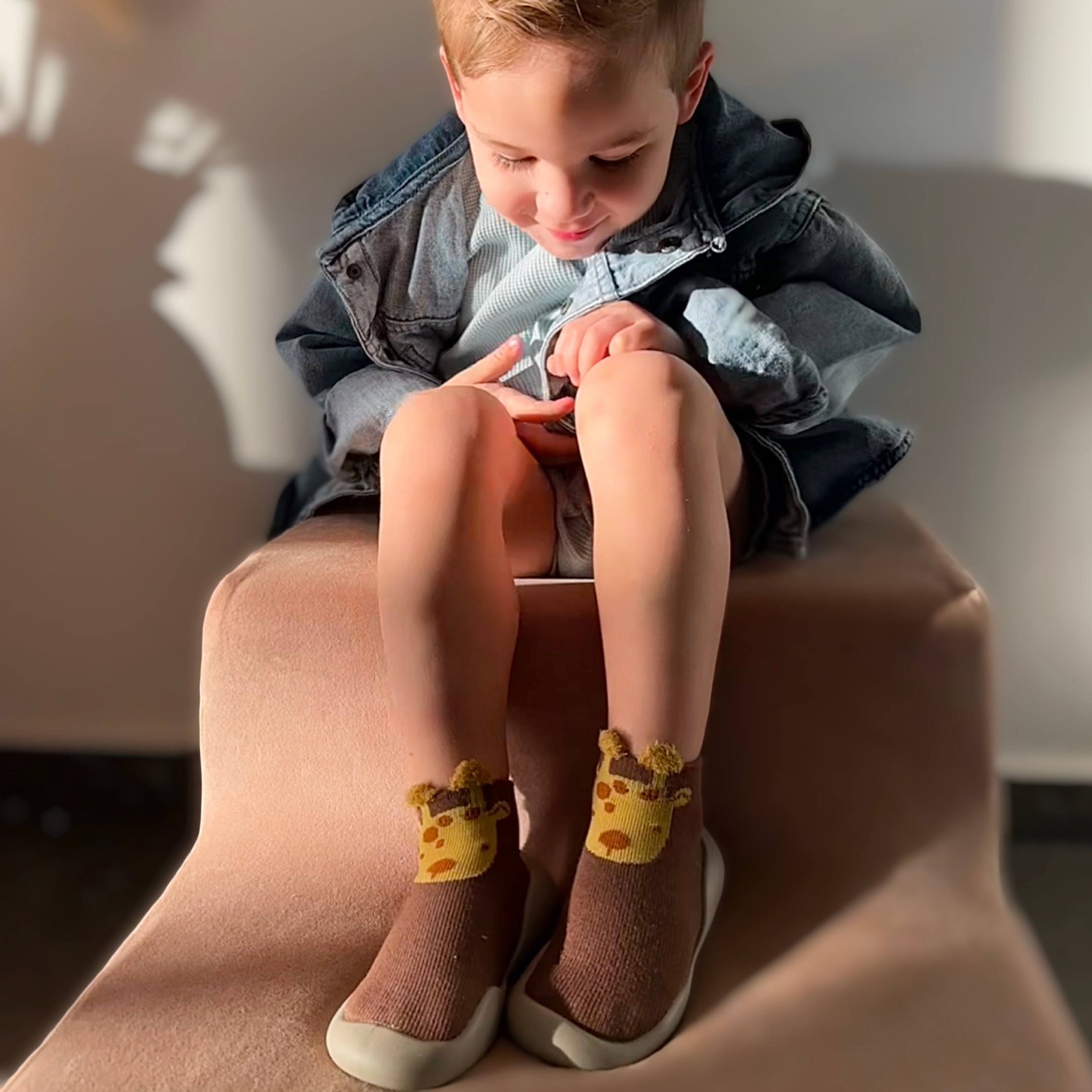Child sitting on a chair wearing giraffe-themed socks, looking down.