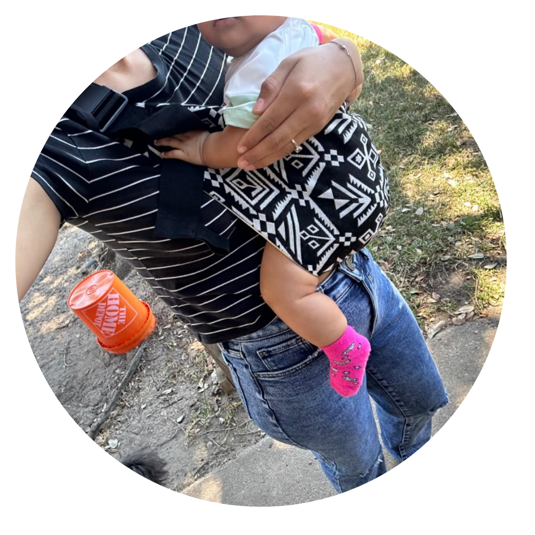 Person holding a baby with a patterned carrier outdoors.