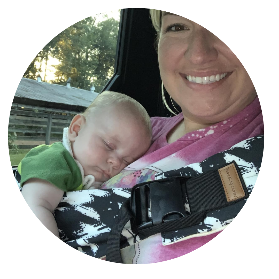 Smiling person holding a sleeping baby in a carrier.