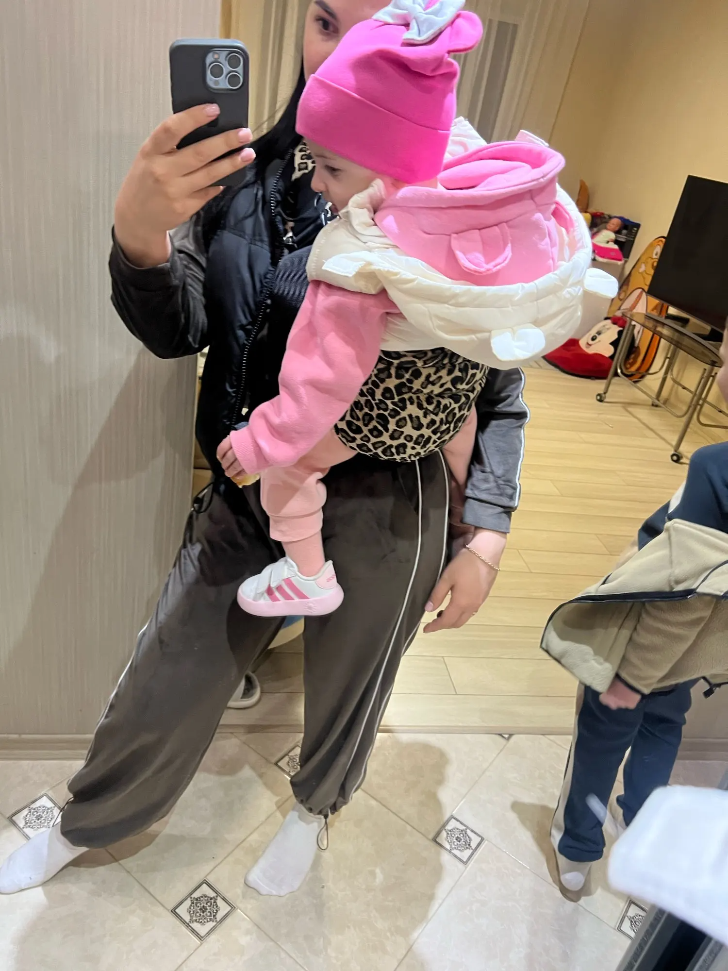 Person taking a mirror selfie holding a child in pink clothing.