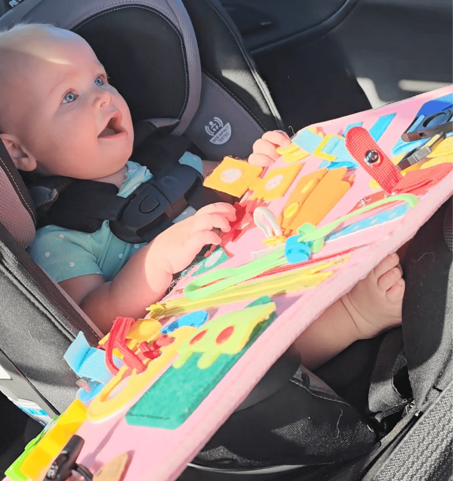 Baby in car seat playing with a colorful activity board.