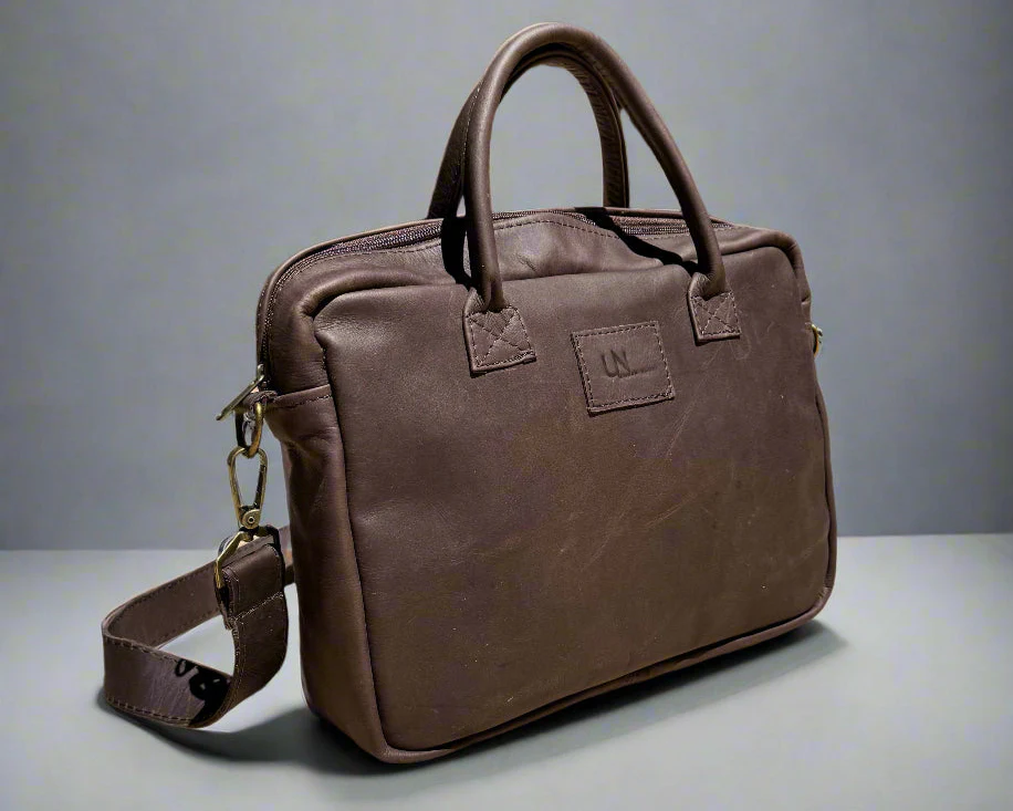 Brown leather handbag with handles and a shoulder strap on a gray background.