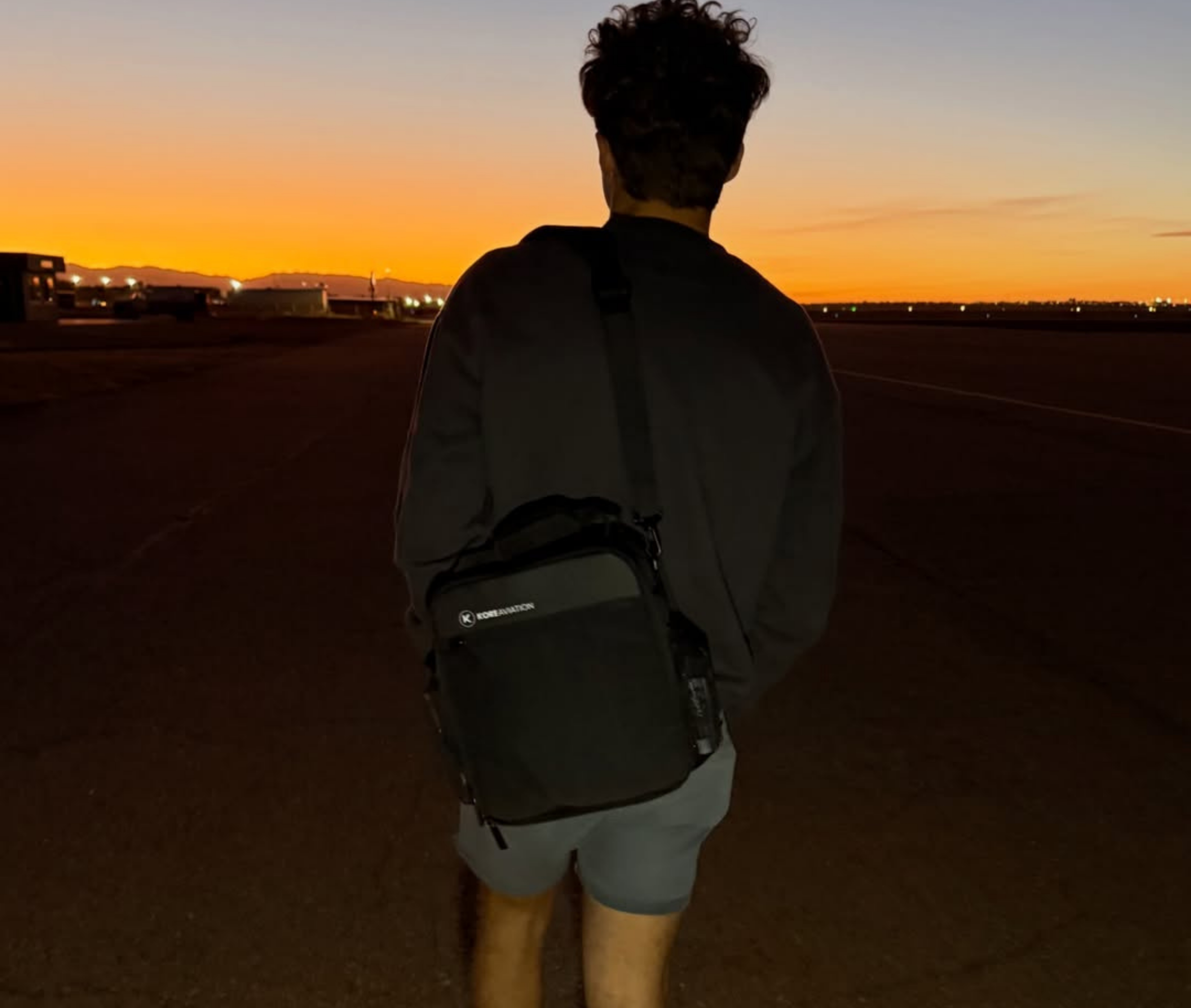 Person with a backpack walking towards a sunset sky.