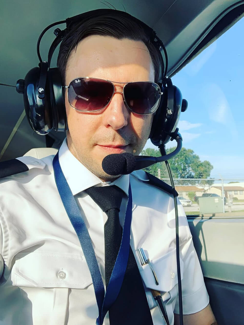 Person in pilot uniform with headset and sunglasses inside an aircraft cockpit.
