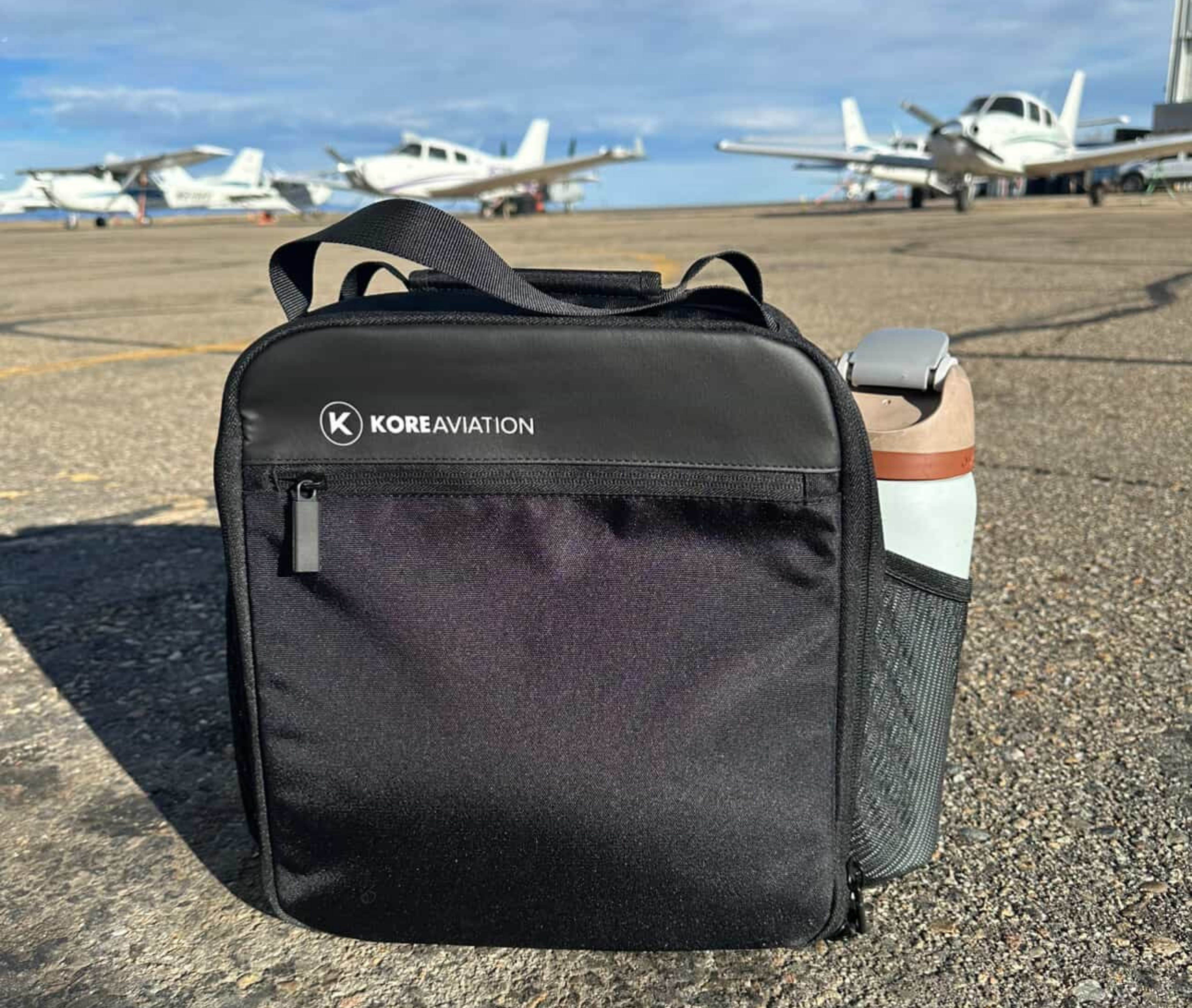 Black bag with 'Kore Aviation' on runway, planes in background.