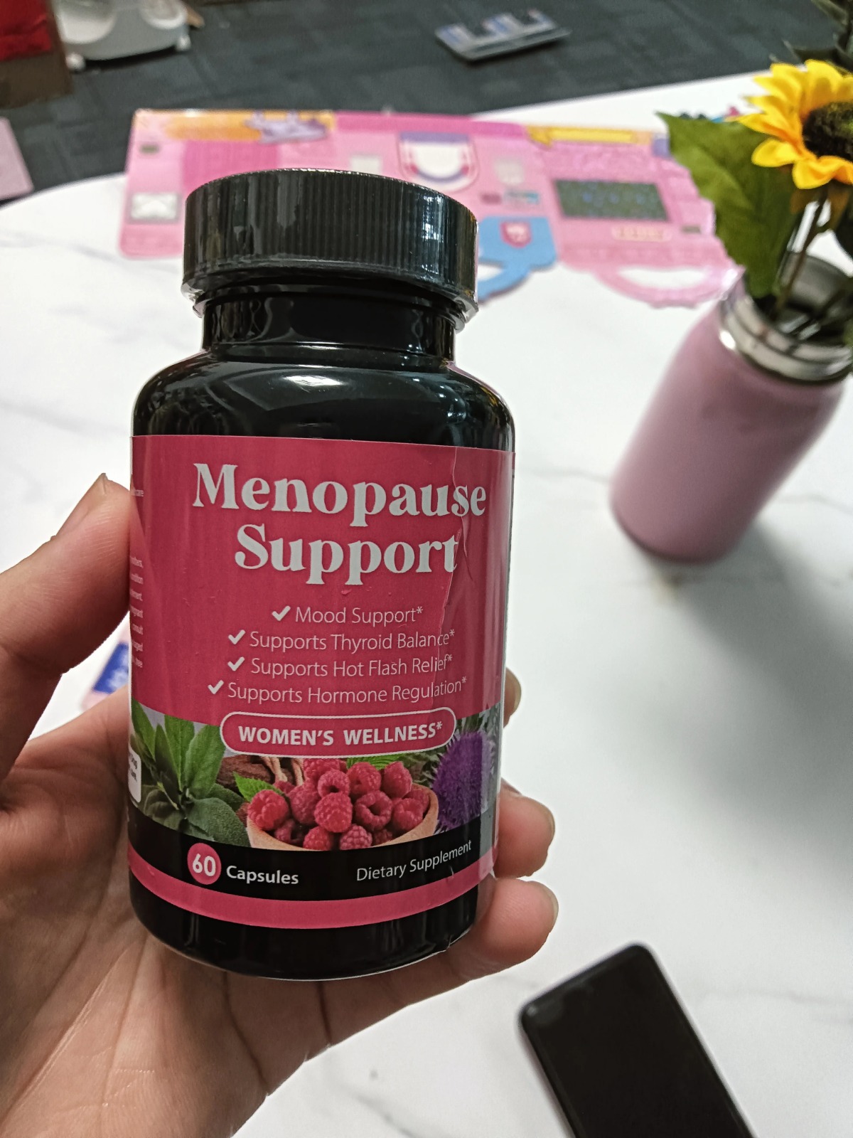 A hand holds a bottle of 'Menopause Support' dietary supplement from the Women's Wellness brand.