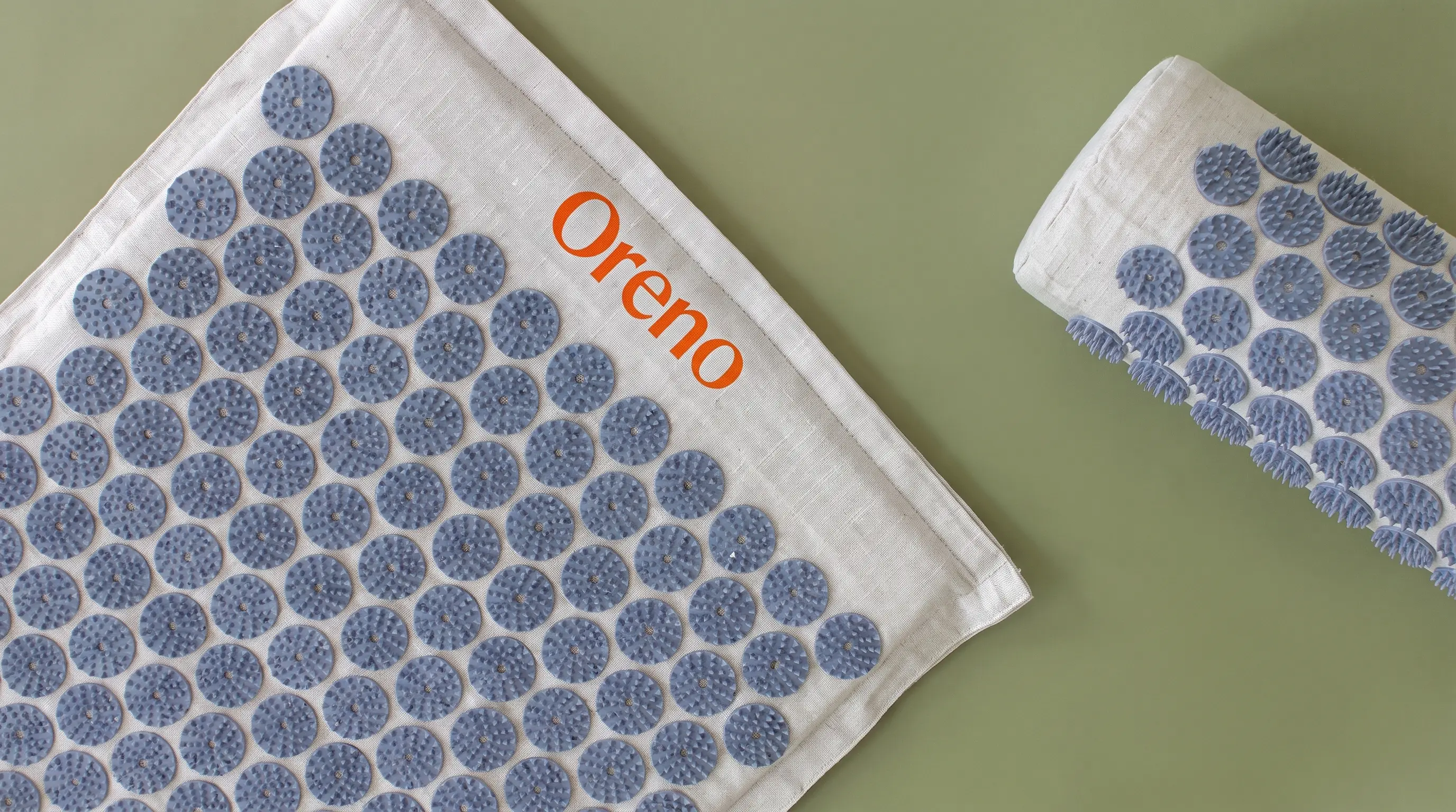 An Orenu brand acupressure mat and a matching rolled pillow on a plain green surface.
