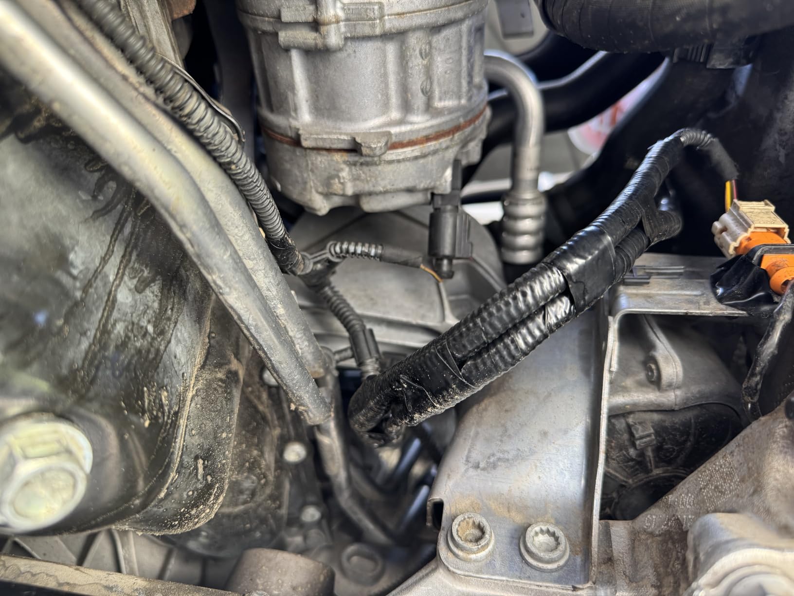 A close-up view of car engine components, including wiring wrapped in black tape and various metal parts.