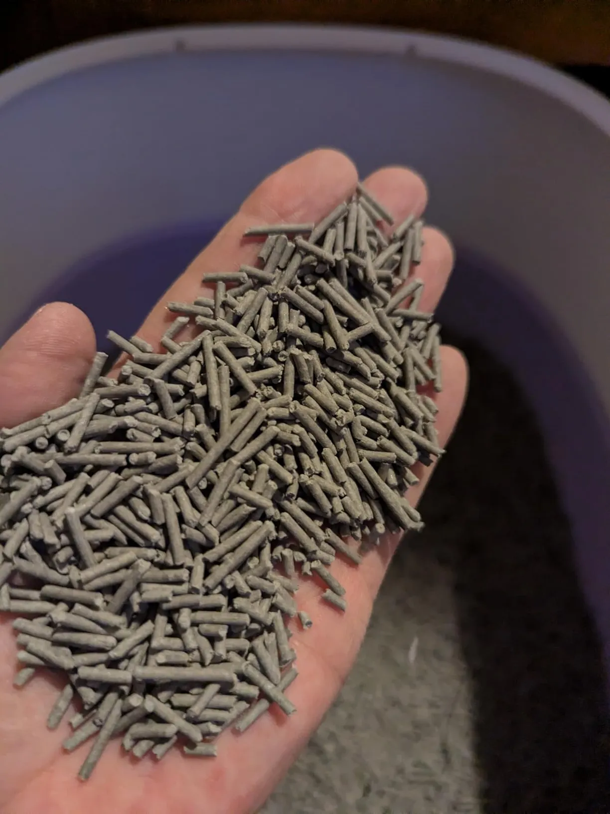 A close-up of a hand holding a handful of gray, pellet-shaped cat litter.