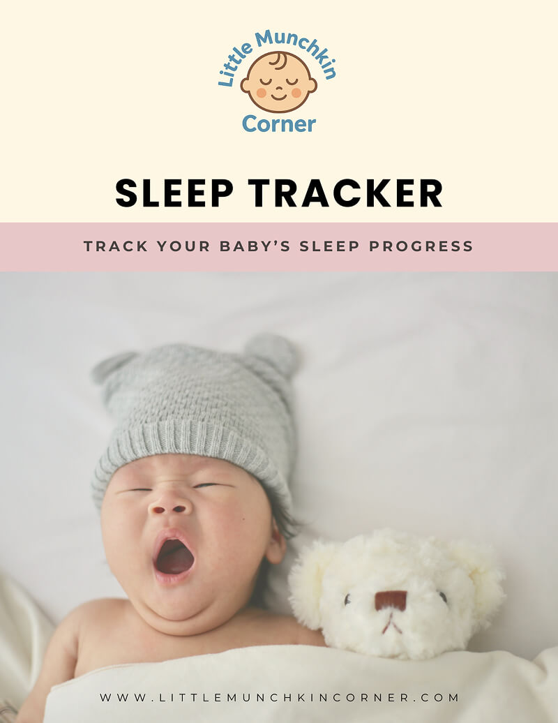 Baby yawning in bed with a teddy bear, wearing a gray knit hat.