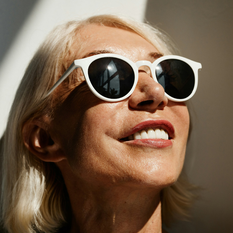 Person wearing white sunglasses, smiling in sunlight.