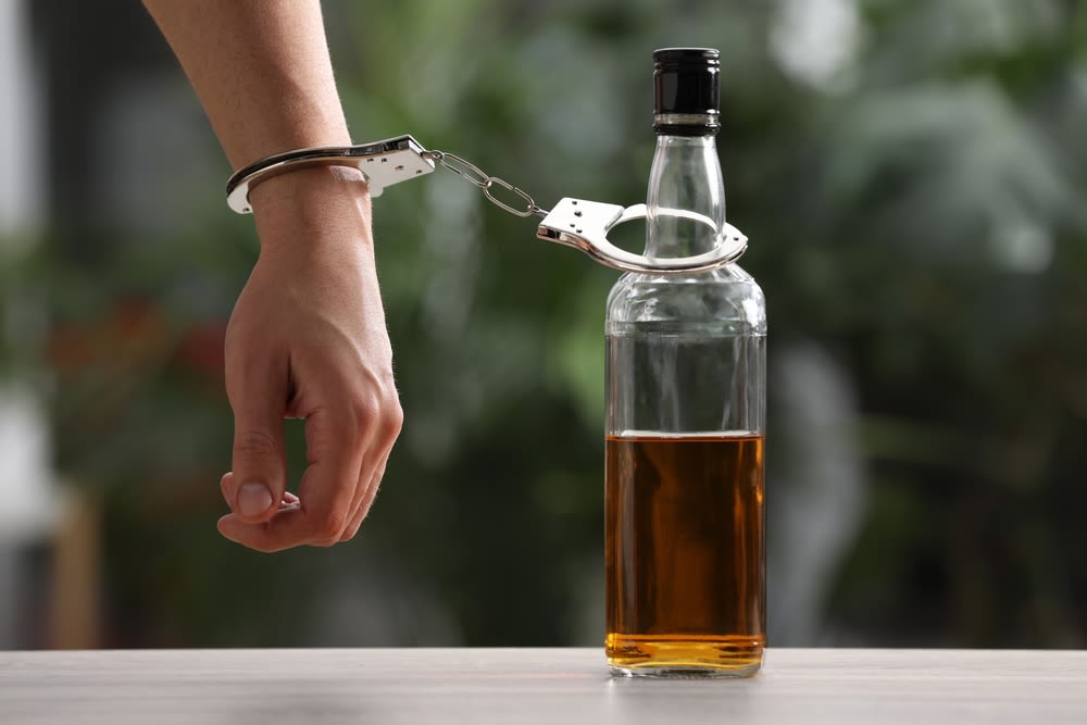 Handcuffed hand attached to a bottle of alcohol on a table.