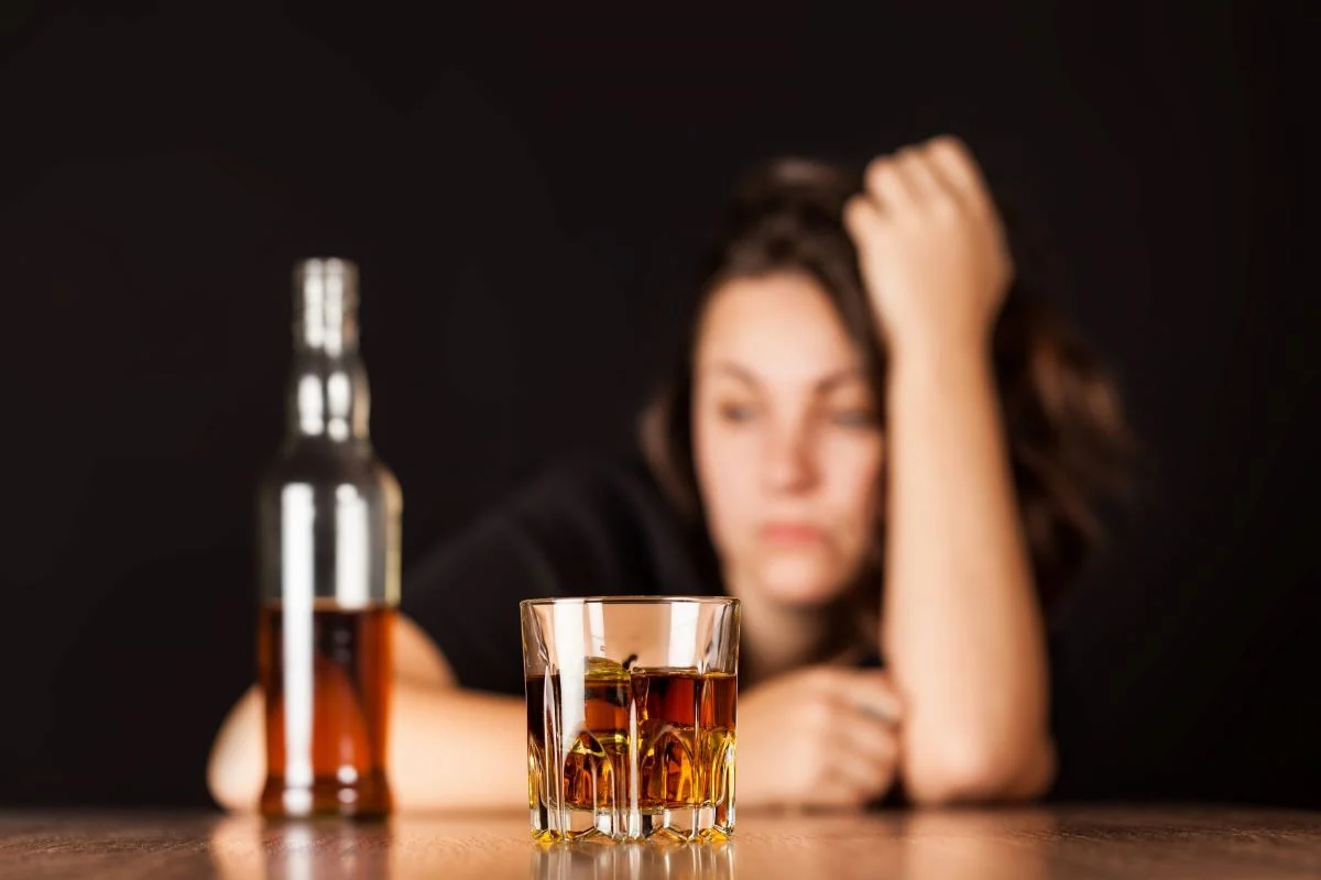 Glass of whiskey and bottle with unfocused person in background.
