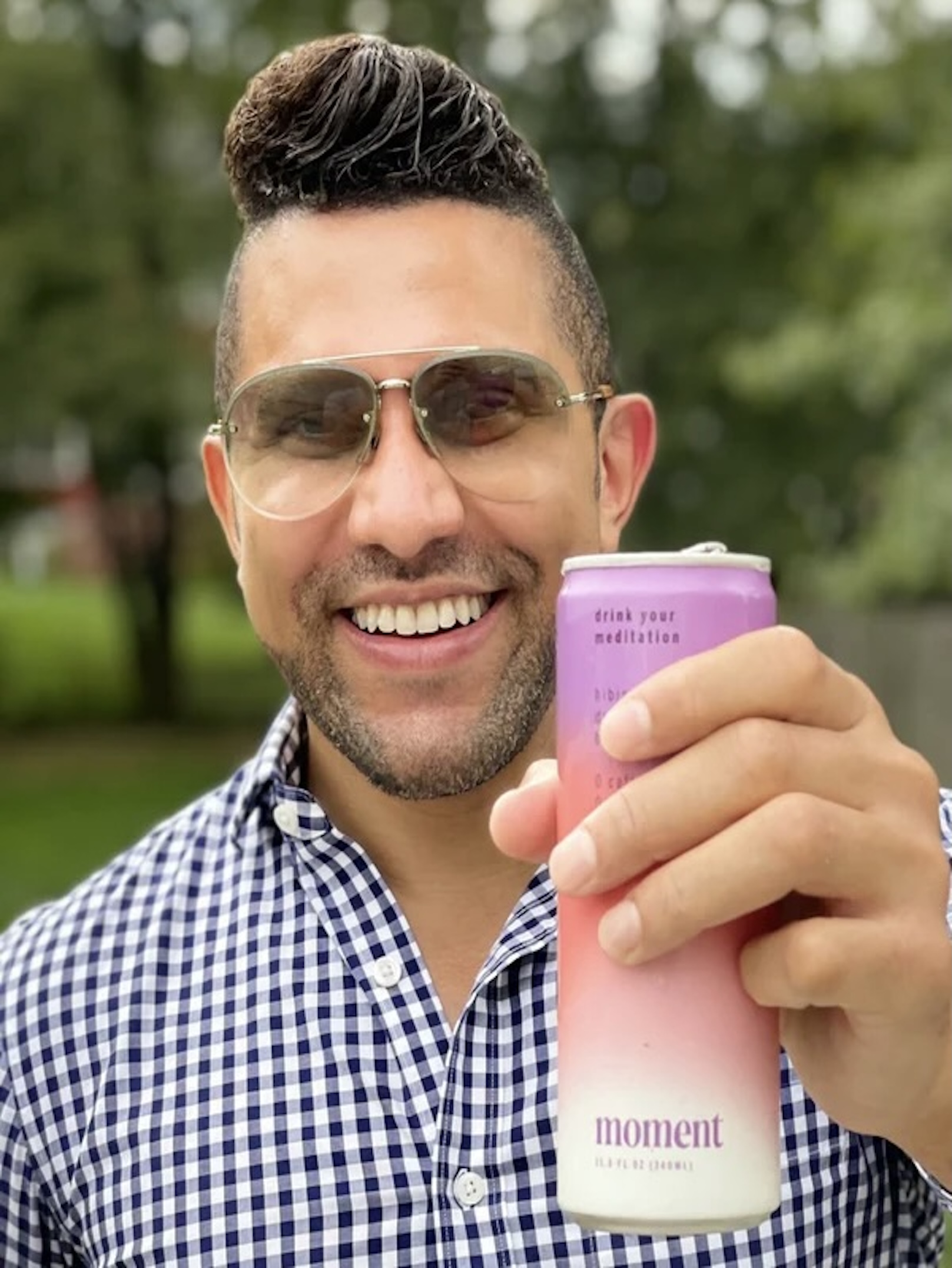 Person smiling and holding a pink can outdoors.