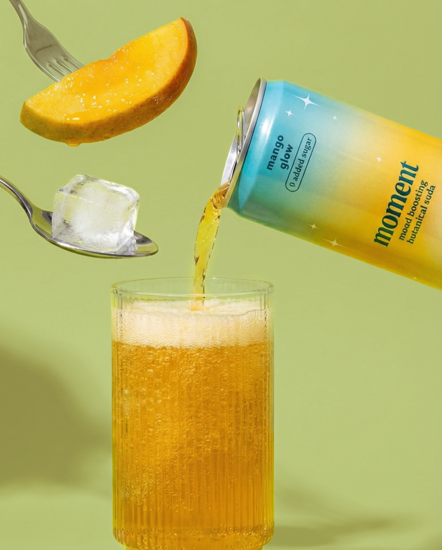 A can pouring drink into a glass with mango slice and ice on forks.