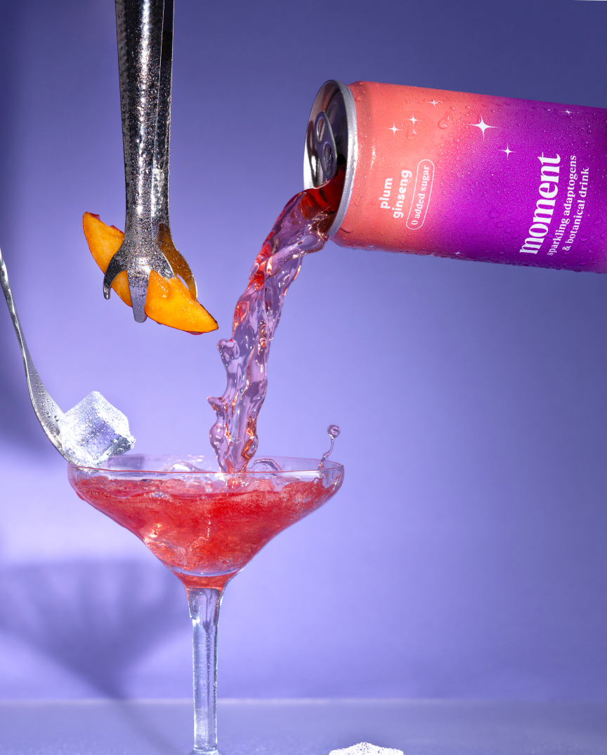 Liquid pouring from can into a cocktail glass with ice and a fruit garnish.