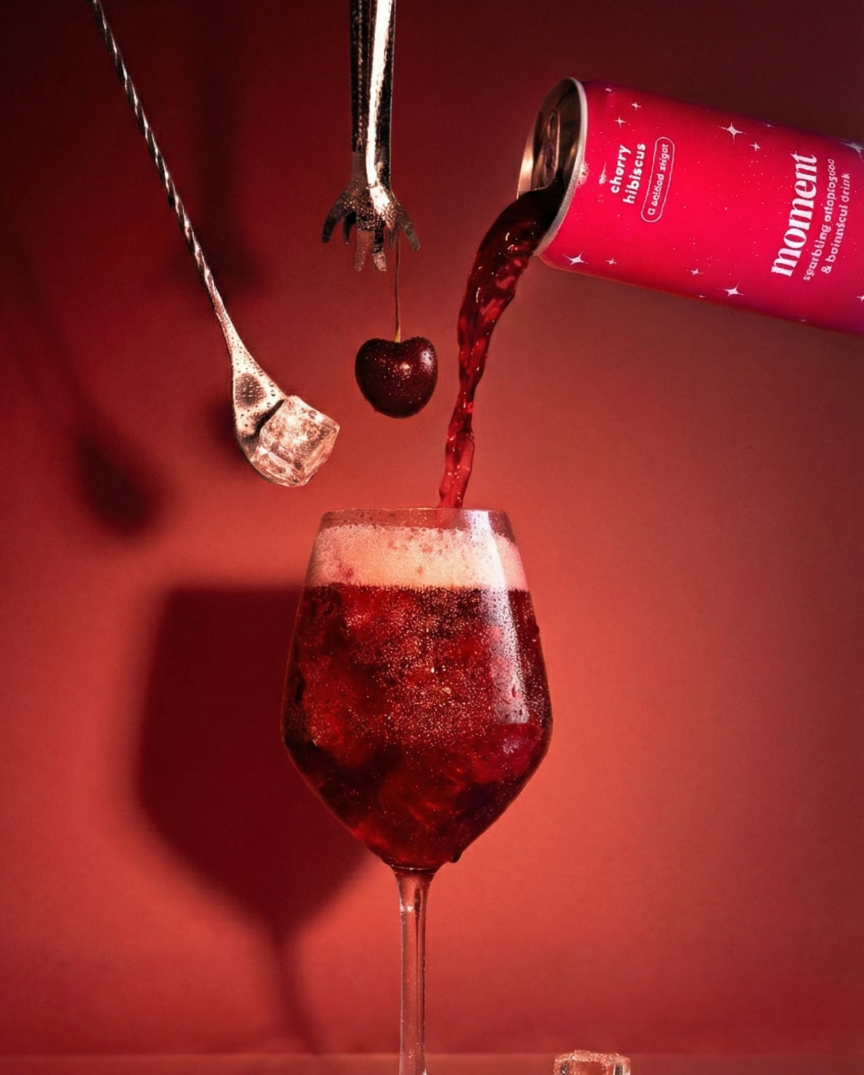 Red drink pouring from can into a glass with cherry and ice.
