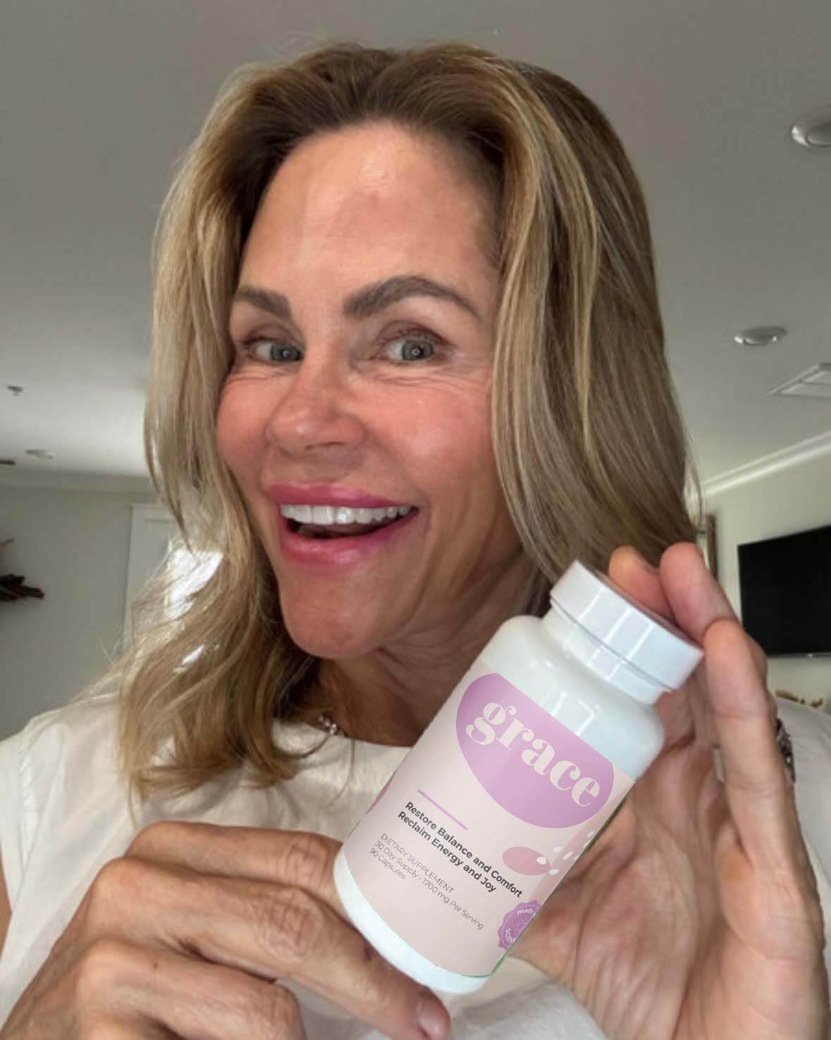 Person smiling and holding a bottle labeled 'grace' in a room.
