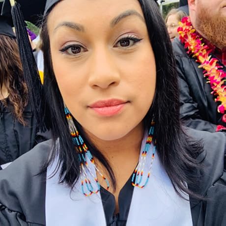 Person in graduation cap and gown, wearing bead earrings, surrounded by others.
