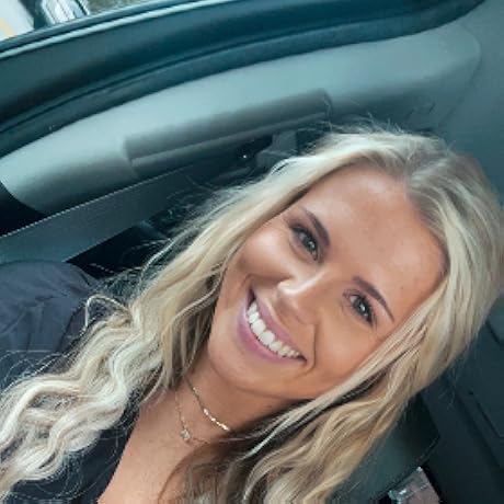 Person smiling inside a car with light hair and wearing a black top.