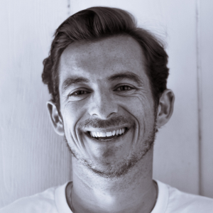 A black and white headshot of a man with short hair smiling warmly at the camera.