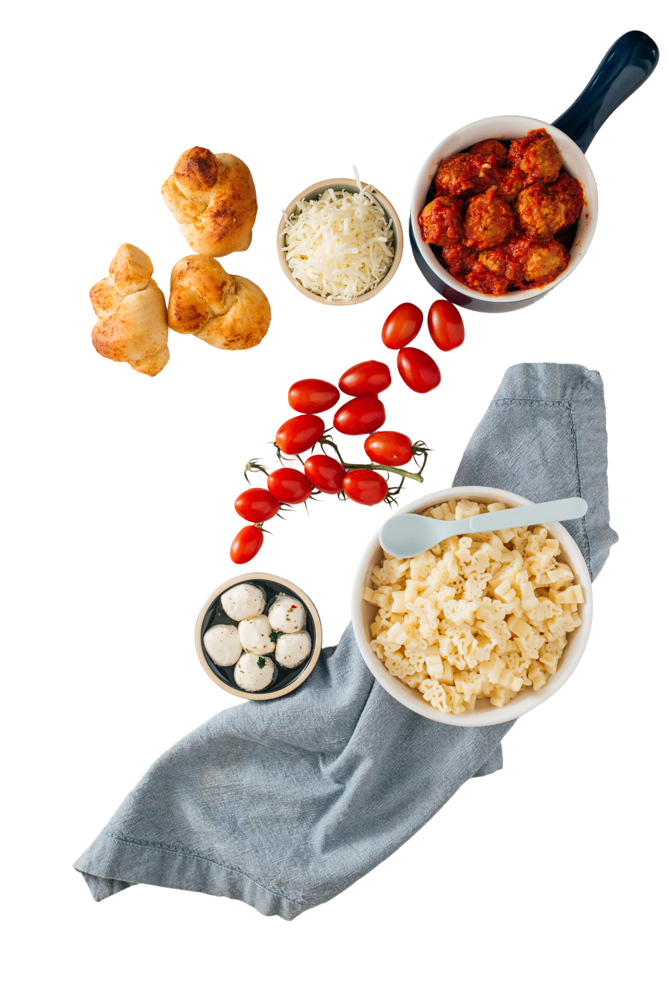 Pasta dishes arranged with meatballs, tomatoes, bread, and cheese on a linen cloth