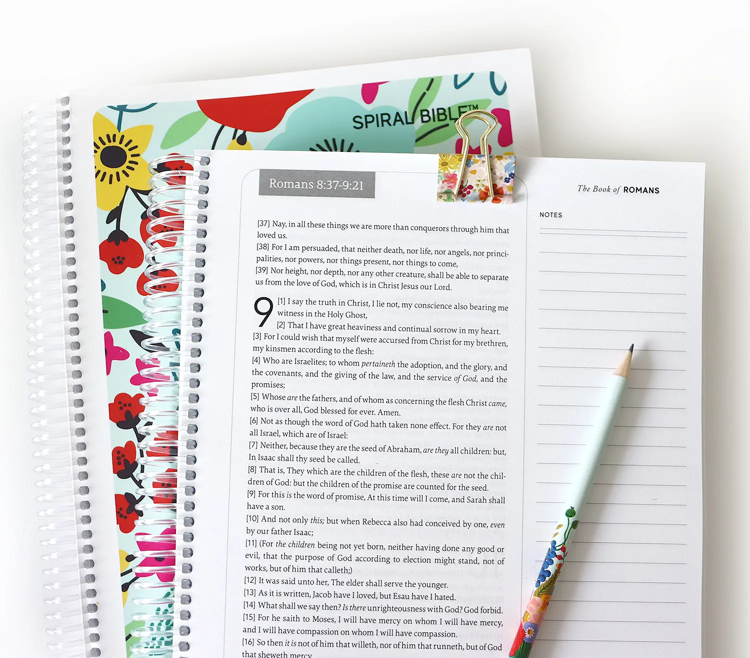 A spiral-bound notebook with text from the Book of Romans and a floral cover.