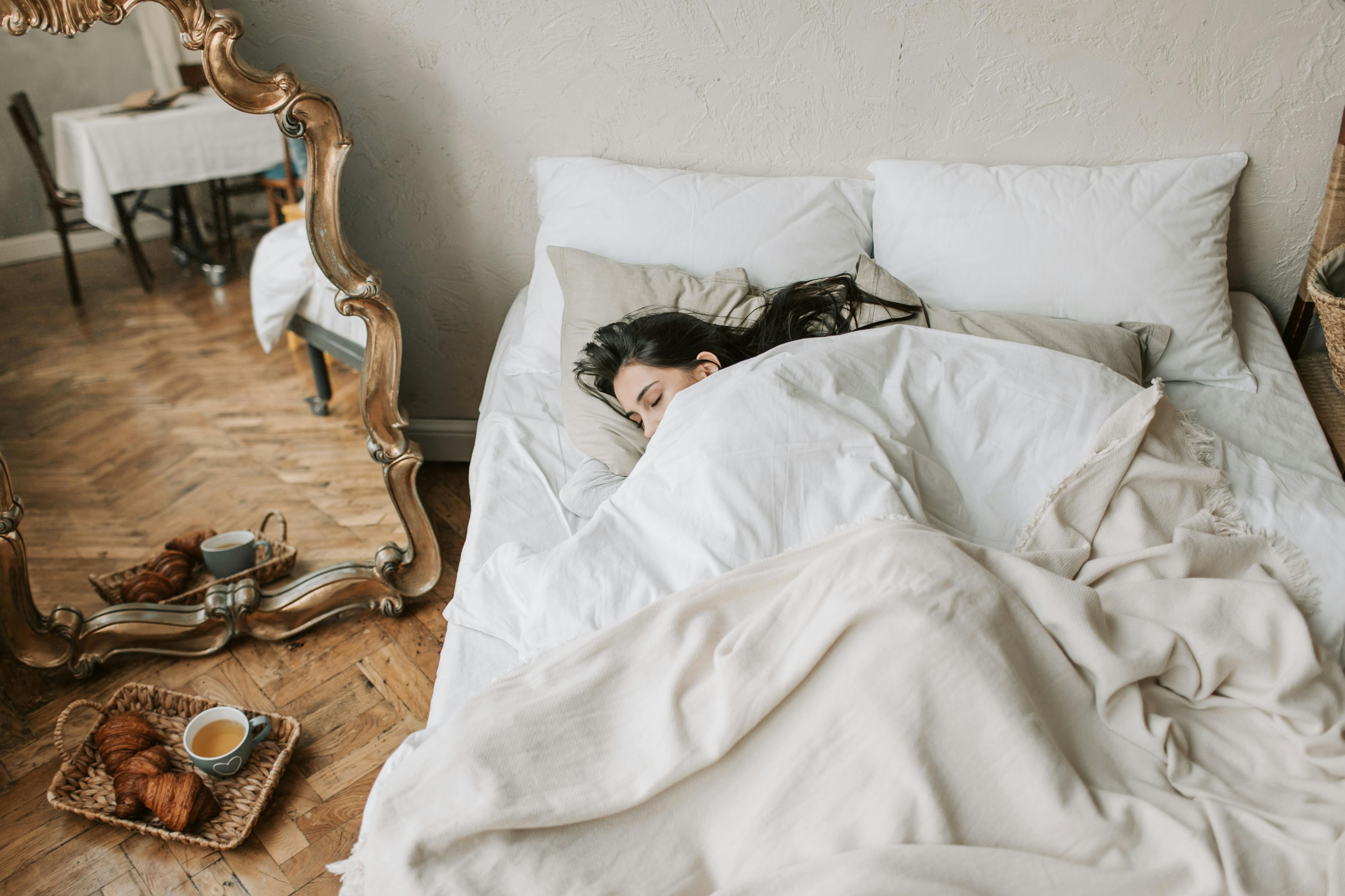 Person sleeping in bed, mirror reflecting table with food.