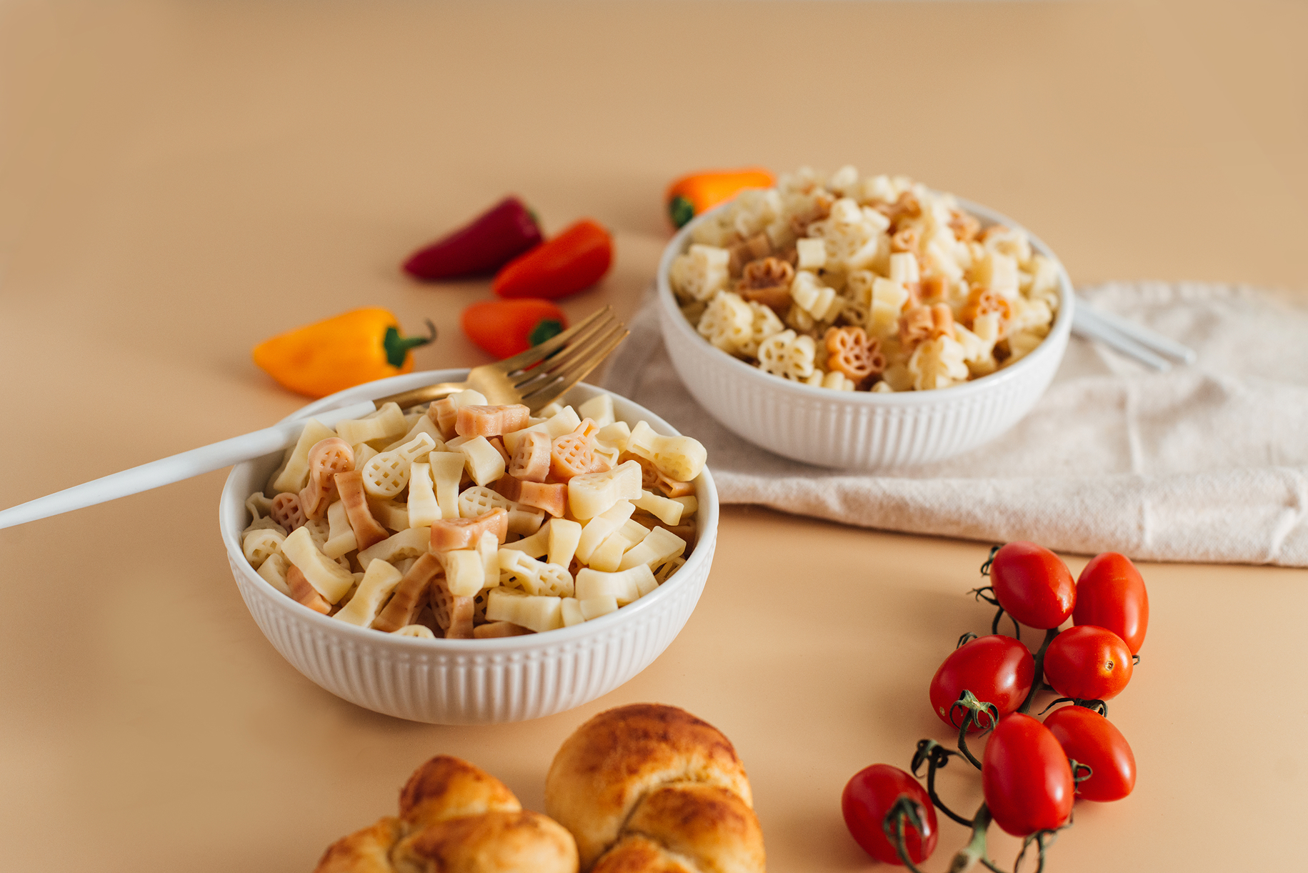 Colorful pasta served in two bowls with peppers, tomatoes, bread, and utensils on a dining table